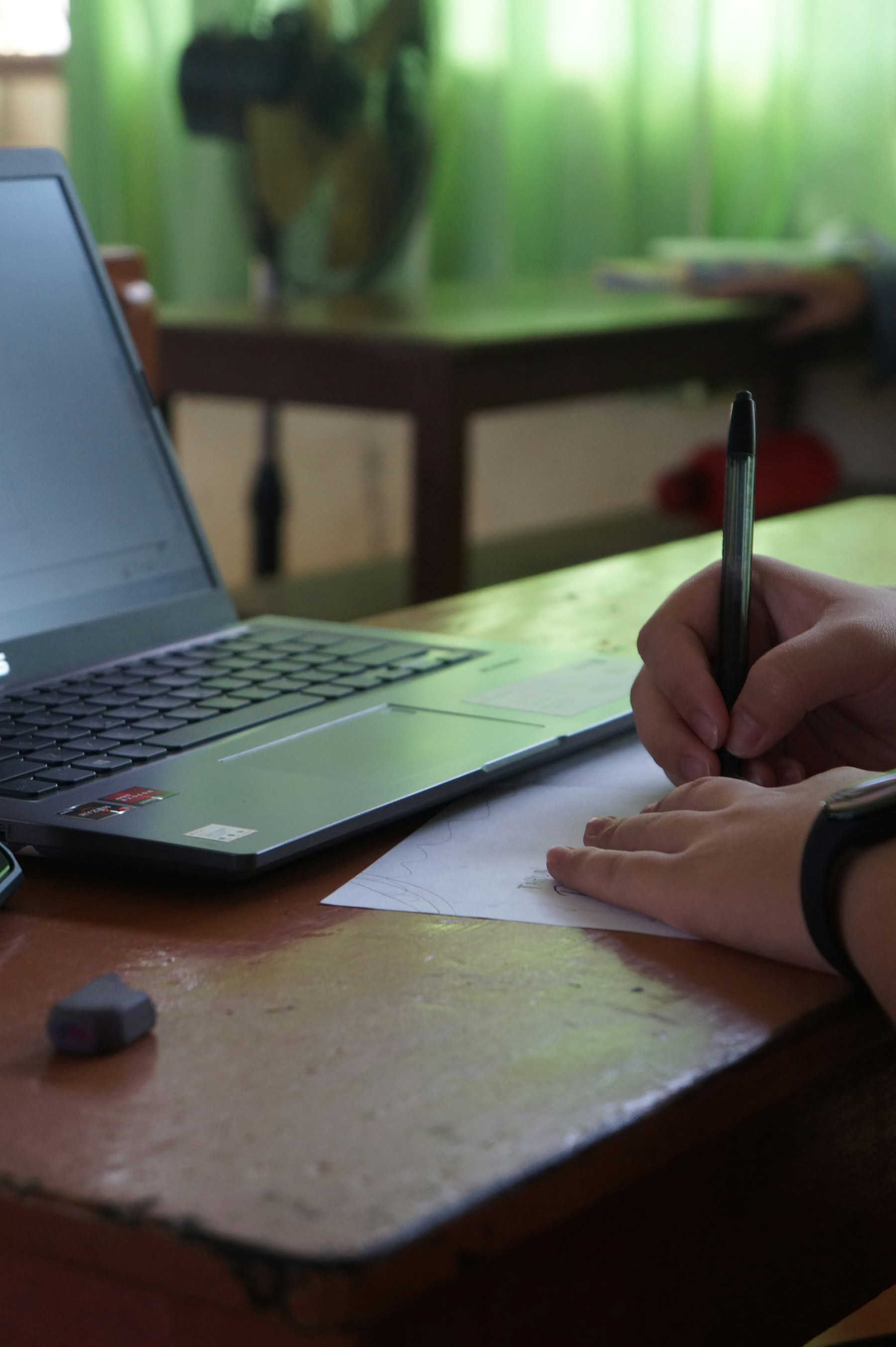 A student writes notes beside a laptop